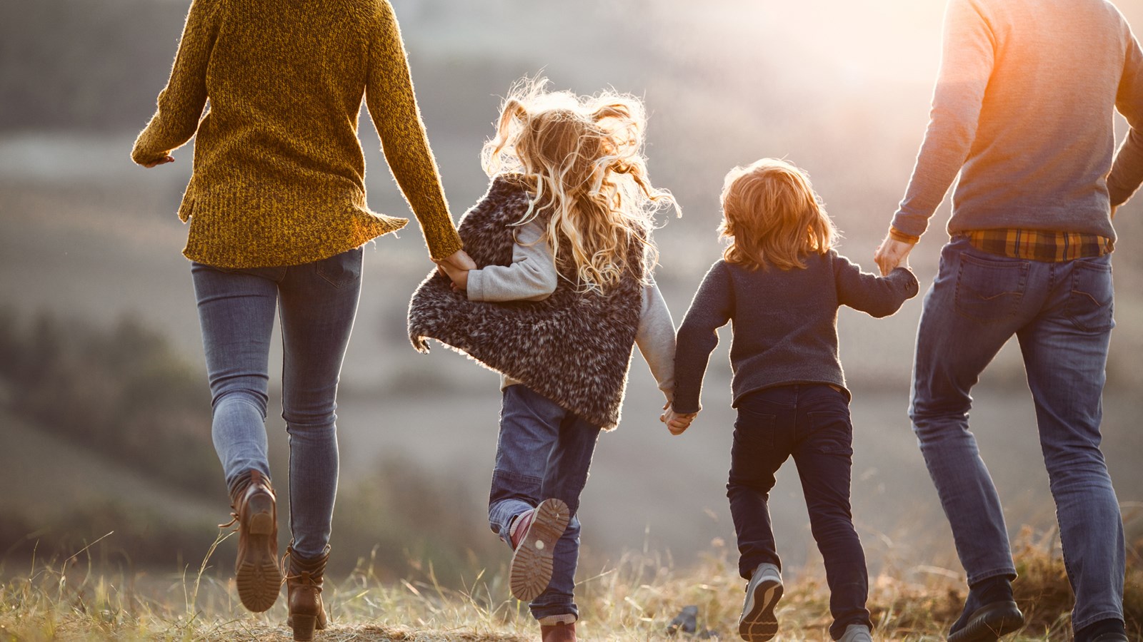 Mamma, pappa, bror och syster håller hand i hand och springer i naturen
